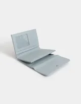 Billetera celeste de cuerina granulada con solapa y tag de metal. Cuenta con broche con botón para cerrado y compartimentos para tarjetas y billetes.
