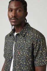 Camisa de manga corta con estampado floral en tonos azul, verde y amarillo. Tiene cuello clásico, cierre con botones y un bolsillo en el pecho.