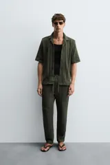 Camisa verde militar de corte relaxed fit, con cuello bowling, manga corta, bajo con aberturas laterales y cierre frontal de botonadura.