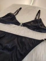 Conjunto de bikini negro con textura acanalada. El corpiño es de corte triangular con breteles regulables y detalle de aro metálico en el centro. La bombacha es tipo colaless con tiras finas regulables en los laterales.