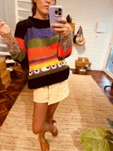 Sweater tejido a rayas horizontales de colores negro, violeta, verde, naranja y amarillo, con detalle de ovejas blancas en el ruedo y mangas tejidas con diseño multicolor.