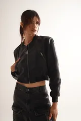 Campera bomber de cuero sintético negro, con cierres y detalles metálicos, y forro interior de tafeta.