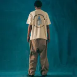 Remera manga corta color crudo, corte oversize, con estampa en la espalda que incluye el logo de la marca Kaboa Industries y la frase "Más barrio que moda".