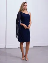 Vestido de fiesta azul marino de seda fría, corte a la rodilla, con un hombro descubierto y aplique de lentejuelas plateadas en el bretel. Incluye una capa de gasa transparente que se sujeta al hombro.