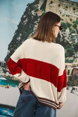 Cardigan de punto grueso, estilo universitario, con bloques de color azul marino, blanco y detalles en rosado y rojo en el cuello y bordes frontales. Presenta botones marrones grandes y el logo 'anthea EST.2016' bordado en el pecho.