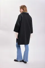 Abrigo negro de paño con corte amplio, cuello camisero, cierre frontal con botones y mangas tres cuartos. Tiene bolsillos laterales y detalle de canesú en la espalda.