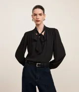 Blusa negra de crepé con cuello con lazo, mangas largas y pliegues en los hombros.