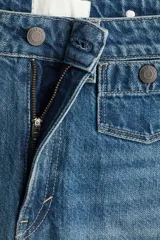 Jeans de tiro alto en denim de algodón rígido, color azul medio con efecto degradado (ombré) que se oscurece hacia el bajo. Corte acampanado (flare) y bajo deshilachado. Presenta bolsillos parche con botón en la parte delantera y trabillas ajustables con botón a los lados de la cintura.