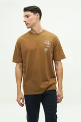 Remera color marrón con cuello redondo y manga corta. Presenta un bordado en el lado izquierdo del pecho con un diseño abstracto y texto.