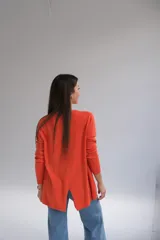 Sweater naranja de tejido de punto, corte recto, cuello redondo y mangas largas. El frente es más corto que la parte trasera y tiene aberturas en la espalda.