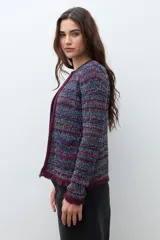Chaqueta corta de tejido bouclé o tweed, sin cuello ni cierre frontal, con ribetes en color bordó. El tejido es una mezcla de hilos en tonos azul marino, rojo/bordó y blanco, creando un efecto jaspeado. Los puños tienen un detalle de flecos en color bordó.