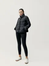 Campera puffer negra ultraligera con cuello alto, cierre de botones a presión, bolsillos laterales y mangas acampanadas. Relleno vegano.