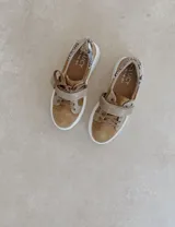 Zapatillas deportivas urbanas con capellada negra, detalles en beige y suela blanca.