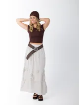 Falda larga de estilo campesino color crudo, confeccionada en algodón italiano con apliques florales al tono. Tiene cintura elastizada y cinto de rafia elastizado desmontable.