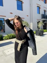 Vestido negro de corte midi, con mangas largas ajustadas y cuello redondo. Incluye cinturón ancho con apliques circulares.