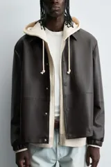 Cazadora de efecto piel color marrón oscuro, corte relajado, con cuello solapa, cierre frontal de botones a presión y bolsillos de vivo en cadera.