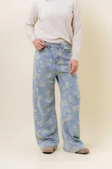 Pantalón de jean de tiro medio-alto, pierna ancha y lavado celeste claro, con estampado floral en tono amarillo pálido.