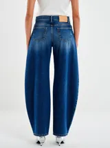 Jeans de denim azul oscuro con efecto degradado (ombré) que se aclara hacia los tobillos. Tienen un corte extremadamente holgado y redondeado (balloon/bomba) y un cordón blanco decorativo colgando del bolsillo delantero.