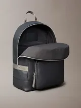 Mochila de piel sintética granulada color negro, con asa superior de tela gris y correas ajustables. Presenta un bolsillo frontal con cierre y el monograma de Calvin Klein en relieve en la parte inferior.