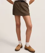 Short pollera de sastrería color marrón, de corte recto y estilo alfatado, con cierre tradicional y bolsillos. Incluye cinturón desmontable de poliuretano.