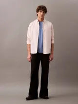 Camisa de manga larga color rosa claro, confeccionada en tejido Oxford de algodón y elastano. Presenta cuello camisero clásico, cierre frontal con botones y logo de Calvin Klein bordado en el pecho. Corte regular.