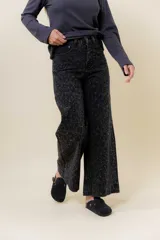 Pantalón de jean negro de pierna ancha y tiro medio-alto, con estampado sutil de leopardo en tono más oscuro y pequeños puntos blancos brillantes.