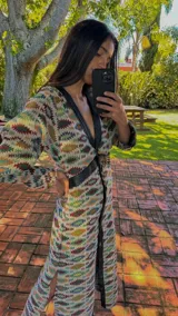 Vestido tipo abrigo con estampado geométrico en tonos azul, marrón y verde, con cuello en V, mangas abullonadas y cierre frontal con botones.