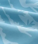 Bermuda de baño masculina de microfibra, color celeste claro, con estampado repetitivo en blanco de palmeras y paisaje tropical. Presenta cintura elástica con cordón ajustable blanco y bolsillos laterales.