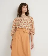 Camisa de gasa color beige con estampado de lunares marrones, cuello mao, mangas 3/4 abullonadas y cierre frontal con botones.