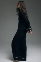 Pijama de dos piezas negro, compuesto por una camisa de manga larga con solapas de muesca, ribetes blancos y cierre de botones, y un pantalón de pierna ancha con elástico revestido en la cintura y ribetes blancos en los puños.