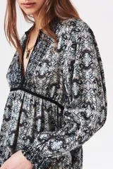 Vestido corto con estampado abstracto en tonos celeste, negro y blanco. Tiene escote en V con ribete de terciopelo negro, mangas largas con puños fruncidos y corte escalonado en la falda.