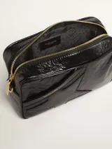Bolso bandolera negro de cuero con efecto desgastado y estrella en relieve. Tiene correa de cuero ajustable y detalles metálicos dorados.