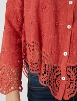 Camisa de algodón color naranja, con bordado suizo y encaje calado. Tiene cuello con solapa, botones frontales, mangas largas con terminación de encaje y ruedo asimétrico con galón de encaje.