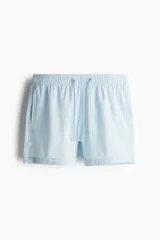 Short de baño celeste con rayas verticales blancas, de sirsaca, con aberturas laterales cortas, elástico en la cintura con cordón ajustable, bolsillos laterales y bolsillo trasero con cierre autoadherente. Suspensor interior de malla.