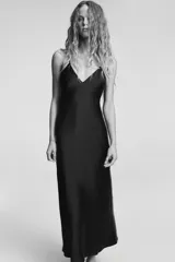 Vestido midi negro de tejido satinado, con escote en pico y tirantes finos ajustables. Presenta un detalle de tiras cruzadas en la espalda descubierta y cierre con cremallera metálica.