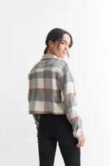 Chaqueta corta a cuadros grises, marrones y blancos, con cuello clásico, cierre abotonado, mangas largas y dos bolsillos con solapa en el pecho.