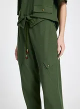 Pantalón jogger verde de tejido de punto con corte recto, cintura con trabillas y cordón ajustable con puntas de madera. Presenta bolsillos laterales con solapa y pespuntes.
