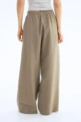 Pantalón de corte holgado color arena, confeccionado en tejido liviano de mezcla de lino. Modelo de tiro alto con elástico revestido en la cintura, cordón para ajustar fino y piernas amplias con bolsillos al bies.