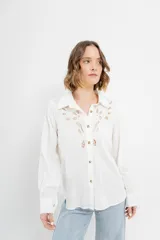 Camisa blanca de voile con bordados calados en el frente, cuello camisero, mangas largas con puños abotonados y cierre frontal con botones. 