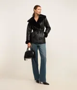 Blazer negro confeccionado en material sintético PU, con cuello y puños de piel sintética, cierre por cremallera y cinturón con hebilla en la cintura.