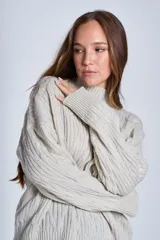 Sweater color crema de punto trenzado, con cuello alto y mangas largas.