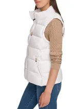 Chaleco blanco acolchado con cuello alto y cierre frontal con cremallera dorada. Tiene bolsillos laterales con cremallera y logo de la marca en el tirador.
