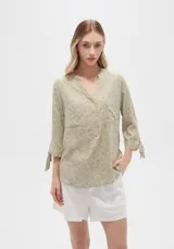 Blusa color verde oliva con estampado de flores blancas, cuello mao, mangas 3/4 con lazo y dos bolsillos frontales.
