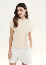 Blusa color crema de tejido acanalado, con cuello redondo y mangas cortas con hombreras.