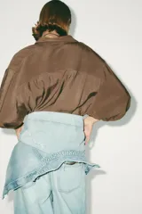 Camisa rosa de cuello solapa y manga corta con vuelta. Bajo asimétrico con aberturas laterales. Cierre frontal con botones ocultos por solapa.