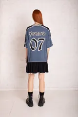 Vestido corto tipo remera deportiva, con parte superior gris con estampado del número 07 y la marca Ragged, cuello en V a rayas blancas y negras, mangas cortas con detalle de encaje y falda negra con volado y encaje en el ruedo.