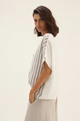 Blusa blanca con rayas verticales grises, corte holgado, mangas cortas con detalle desflecado y cuello redondo.