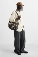 Bolso de hombro tipo bandolera, confeccionado en tejido de algodón con estampado abstracto en tonos blanco y negro. Cuenta con un compartimento principal con cierre de cremallera, un bolsillo interior con cremallera y asa de hombro ajustable.