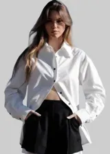 Camisa blanca de corte asimétrico con cierre lateral y mangas largas.