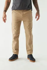 Pantalón chino color beige, de corte slim, con bolsillos laterales y traseros. Se ajusta a la cintura con cinturón de cuero marrón.